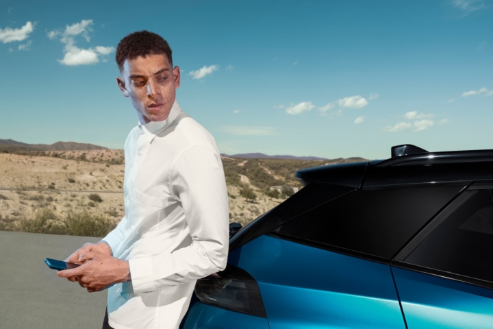 Homme utilisant son smartphone devant une Peugeot 2008 hybride – véhicule connecté à louer à Valence, Drôme et Ardèche